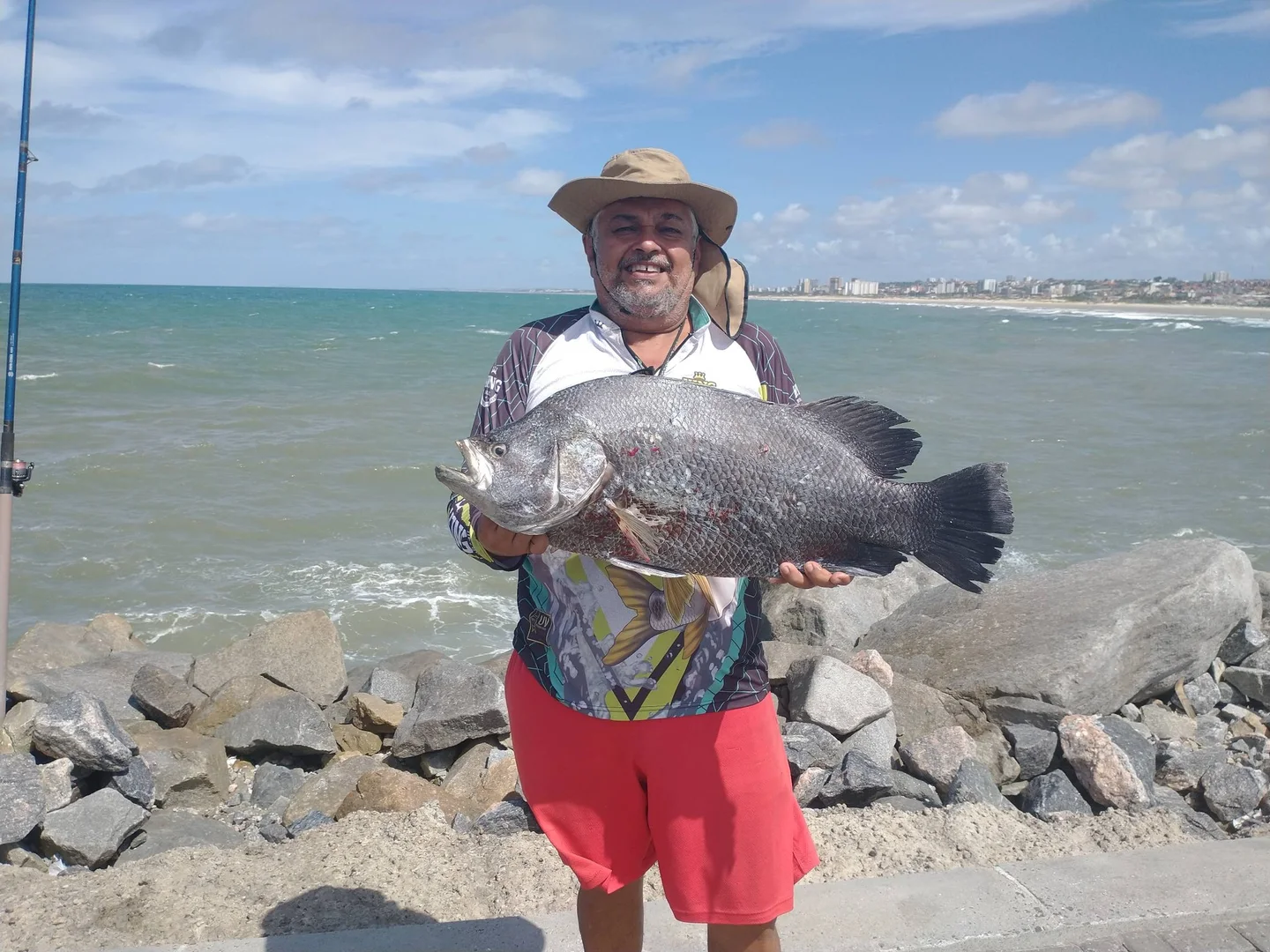 Daniel, pescador que atende a Pescaronha, segurando um peixe à beira-mar